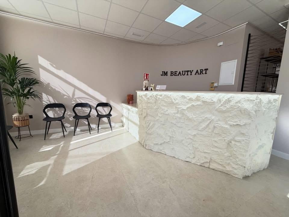 Recepción de JM Beauty Art: mostrador curvo revestido de piedra blanca tallada, con el rótulo del centro en la pared